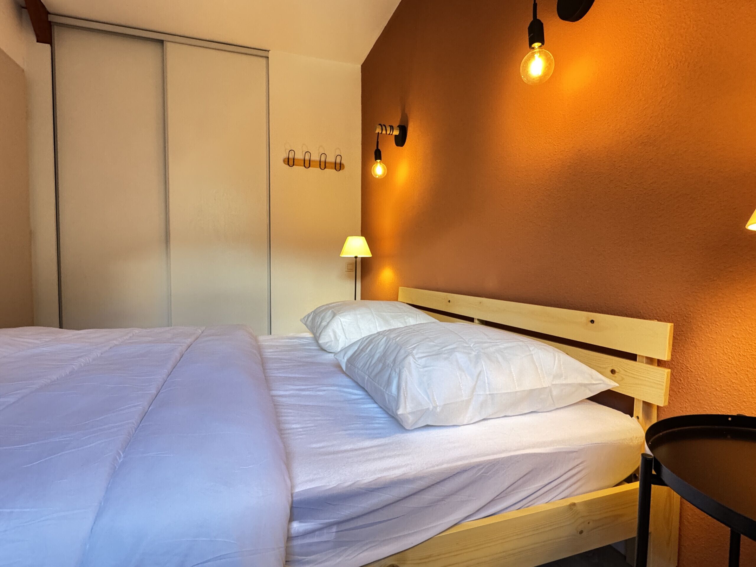 A hotel room with a wooden bed, white bedding, a small round table, and wall-mounted lamps.