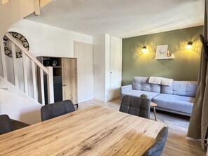 A modern living room with a wooden dining table, grey sofa, and a staircase leading to a loft area. - Joli duplex 5P. Parking & balcon (Cauterets)