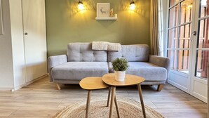 A living room with a grey sofa, two wall-mounted lights, a framed picture, and a small table with a plant.
