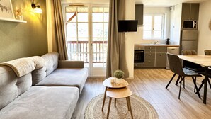 Un salón moderno con un sofá, una pequeña mesa redonda con una planta y un televisor montado en la pared.