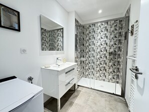 A modern bathroom with a white vanity, a large mirror, a shower with patterned tiles, and a glass door.