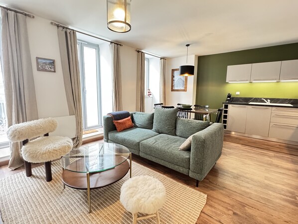Un salon moderne avec un canapé vert, une table basse en verre et un fauteuil blanc moelleux.
