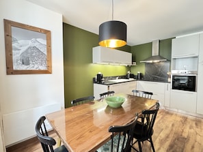Une cuisine moderne avec des meubles blancs, une table à manger en bois et un luminaire suspendu.