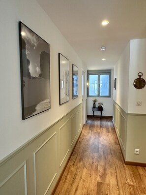 A hallway with wooden flooring, white walls, and framed artwork.