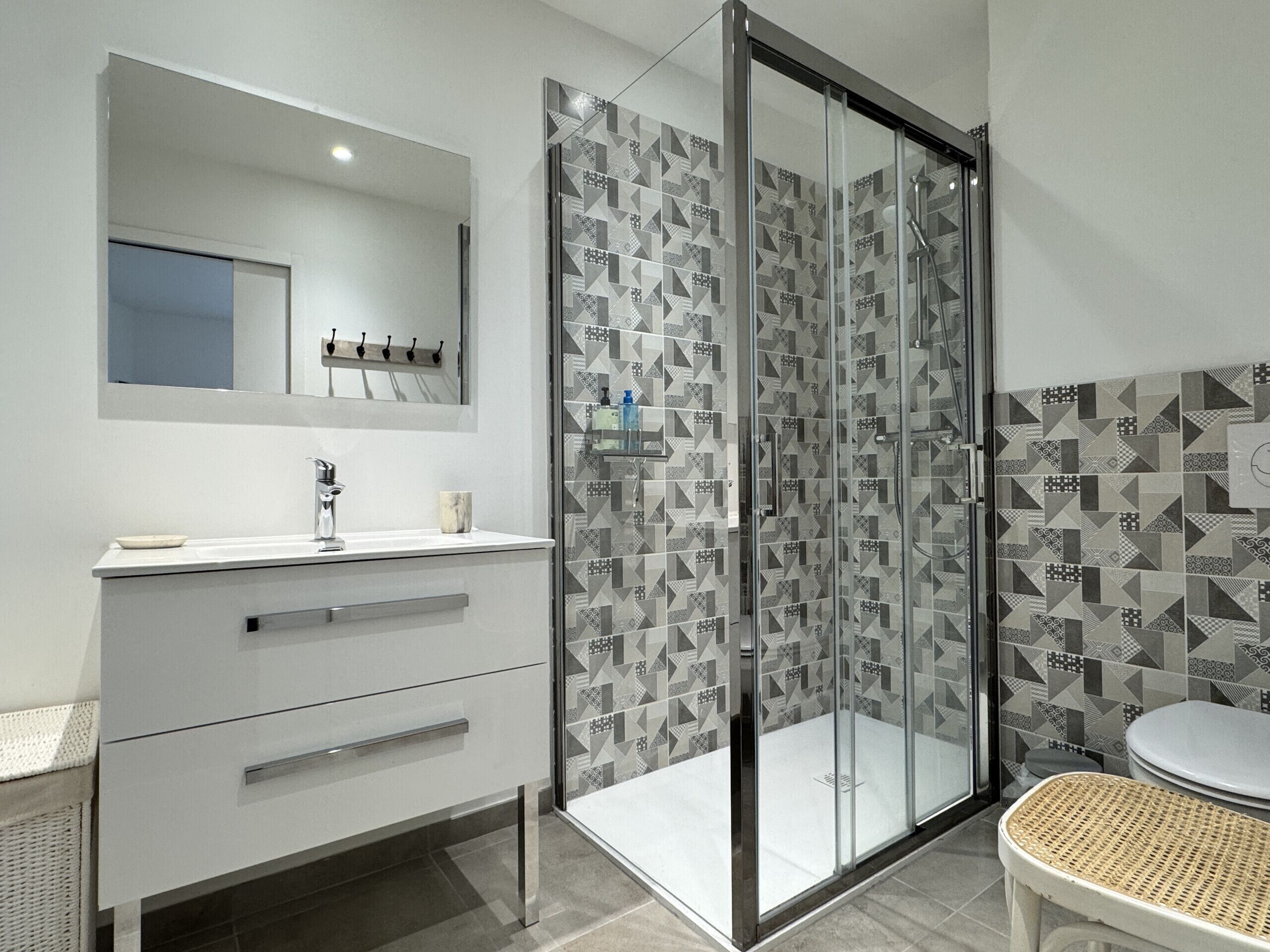 A modern bathroom with a glass-enclosed shower, a white vanity with a mirror, and patterned tiles on the walls.