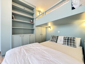 A bedroom with a bunk bed, a large wardrobe with multiple shelves, and bedside lighting.