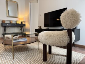 Un salon moderne avec une table basse en verre, un fauteuil moelleux, une console en bois foncé et un téléviseur à écran plat.