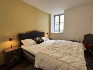 A bedroom with a bed, a nightstand, a lamp, a chair, and a window. - Plein centre. Bel apt 4pièces de 80m2 pour 6 pers. (Cauterets)