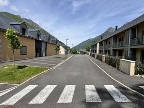 A street view of a residential area with modern buildings, a crosswalk, and a mountain backdrop. - Bel apt 85m2 8P. Parking. Balcon (Cauterets)