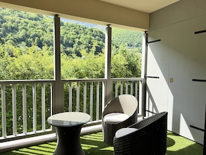 A balcony with a view of a forested hillside, wicker furniture, and a white door.