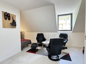 A small, modern room with a bed, two black chairs, a small table, and a window providing natural light.