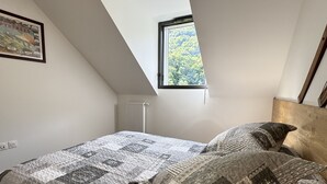 Une chambre avec un plafond en pente, une fenêtre donnant sur les arbres, un radiateur et un lit recouvert d’une courtepointe matelassée et agrémenté de deux oreillers.