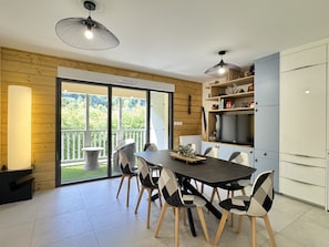 A modern kitchen with a dining area, featuring a large window, a built-in TV, and a wooden accent wall.