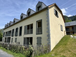 Un edificio de varios pisos con techo plano, múltiples ventanas con contraventanas y un borde de piedra a lo largo del costado.