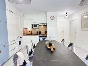 A modern kitchen with white cabinets, a microwave, and a sink. There is a dining table with chairs and a potted plant on it. - Bel apt 85m2 8P. Parking. Balcon (Cauterets)