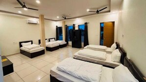 Une chambre d’hôtel avec quatre lits disposés en forme de U, des ventilateurs de plafond et un appareil de climatisation.