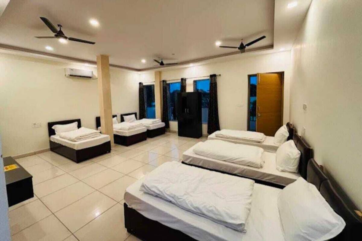 A hotel room with four beds arranged in a U-shape, ceiling fans, and an air conditioning unit.