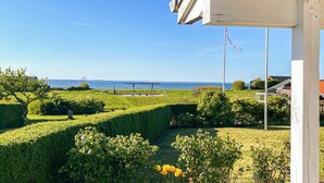 A garden with a view of the sea, a flagpole, and a building with a white exterior.