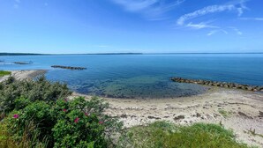 A coastal landscape with clear blue water, sandy beach, and rocky outcrops.