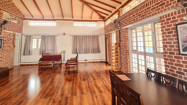 A spacious room with wooden flooring, a high ceiling with exposed beams, brick walls, and large windows. - The Windsor Villa (Trimbak)