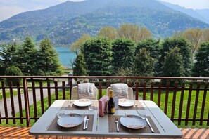 Tavola imbandita per due con bottiglia di champagne, piatti e posate, con vista su un lago e dolci colline boscose.