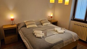 Una cama bien hecha con una colcha estampada, dos lámparas de noche y una ventana con persianas.
