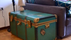 A green vintage suitcase with metal accents, placed on a tiled floor next to a sofa with patterned cushions.