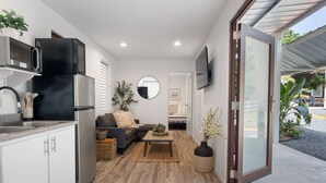 Una cocina moderna con un refrigerador negro, un microondas y un lavamanos. Hay una zona de comedor con un sofá y una mesita de centro.