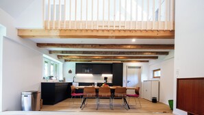 A modern kitchen with a central island, wooden beams on the ceiling, and a dining area with a table and chairs.