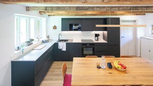 A modern kitchen with a wooden dining table, black cabinets, and a window overlooking the room.