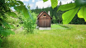 A wooden cabin with a pitched roof, surrounded by lush greenery and a clear sky.
