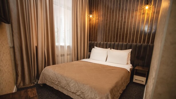 A neatly made bed with a beige bedspread, a wooden headboard, and a bedside table with a drawer. - Central Budget GH  (Baku)