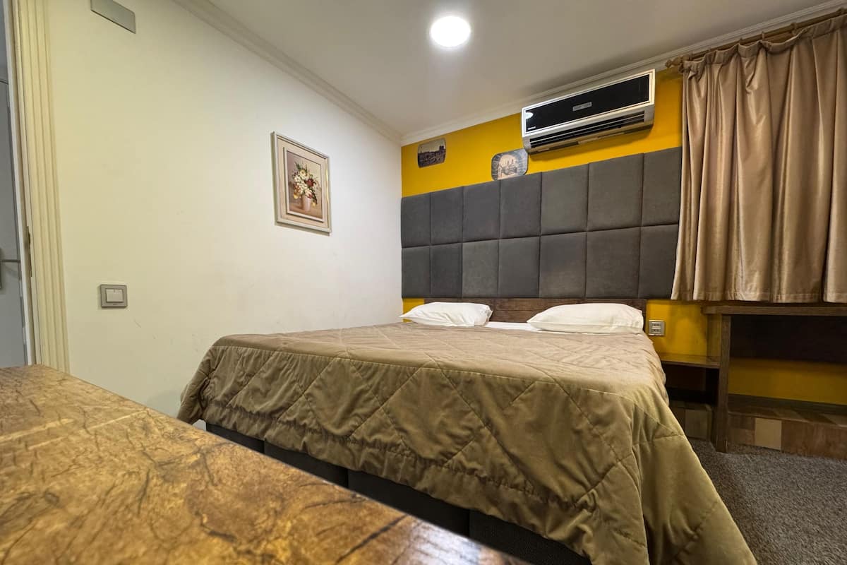 A hotel room with two beds, a headboard, an air conditioning unit, a wall clock, and a curtain.