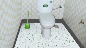 Un baño con inodoro, un cepillo de limpieza verde y una pequeña ventana sobre el inodoro.
