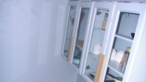 Una pequeña cocina con un refrigerador, una mesa de madera y una ventana con estantes.