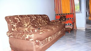Un sofá marrón con estampado paisley en una habitación con suelo de baldosas y una ventana con cortinas naranjas.