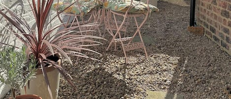 A courtyard with a metal table and chairs, potted plants, and a clock on a post.