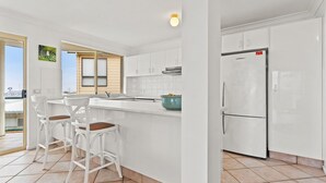 A modern kitchen with white cabinetry, a large island with bar stools, a built-in oven, and a refrigerator. - Shelly Vista - Beach Days and Poolside Afternoons (East Ballina)