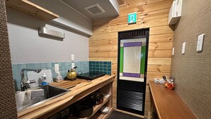 A compact kitchen with a sink, a kettle, and a small countertop. There is a door with a window and a sign above it. - BeachHouseNumazu (Numazu)
