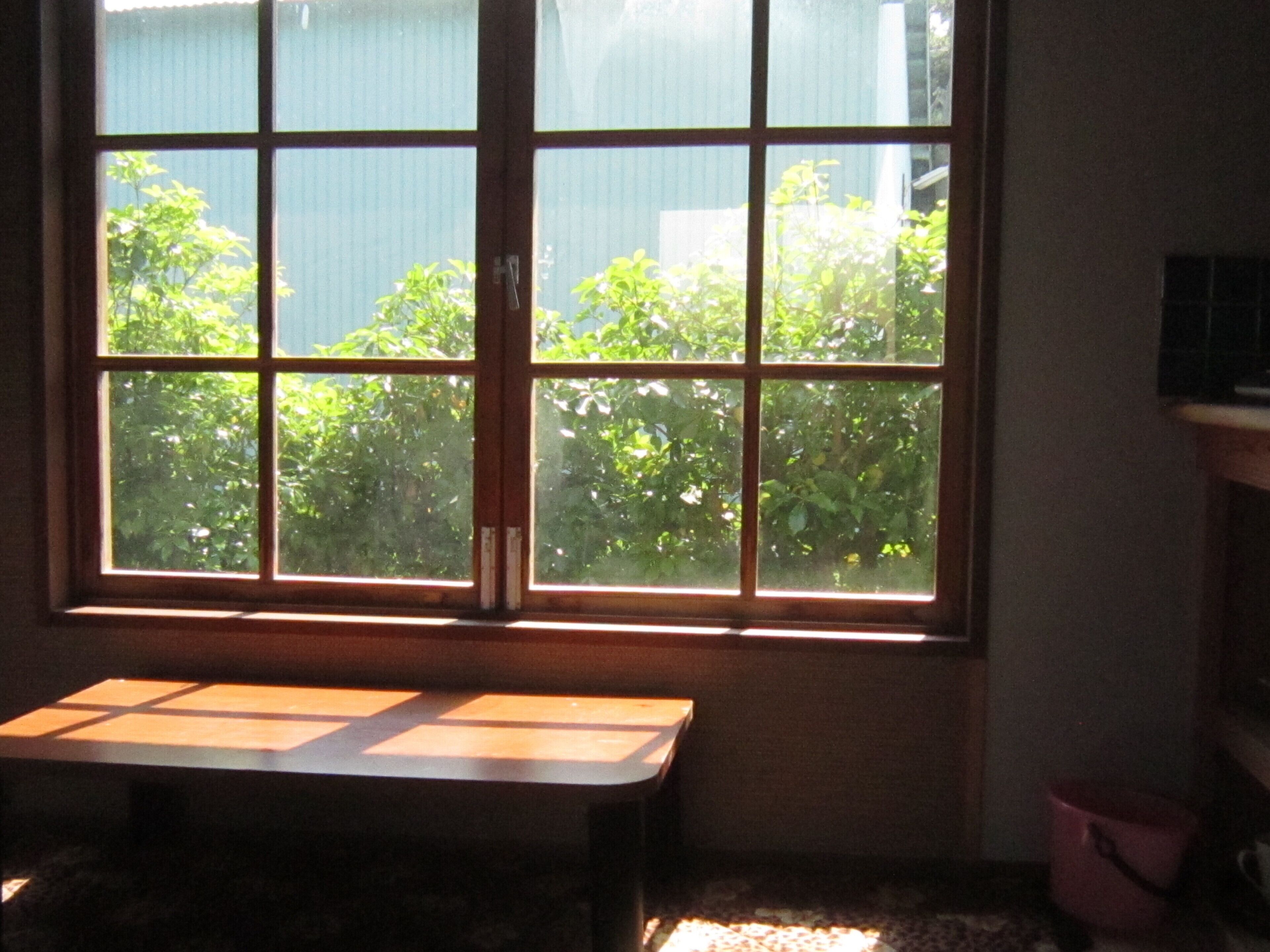 Une pièce avec une grande fenêtre, une table en bois et un seau rose.