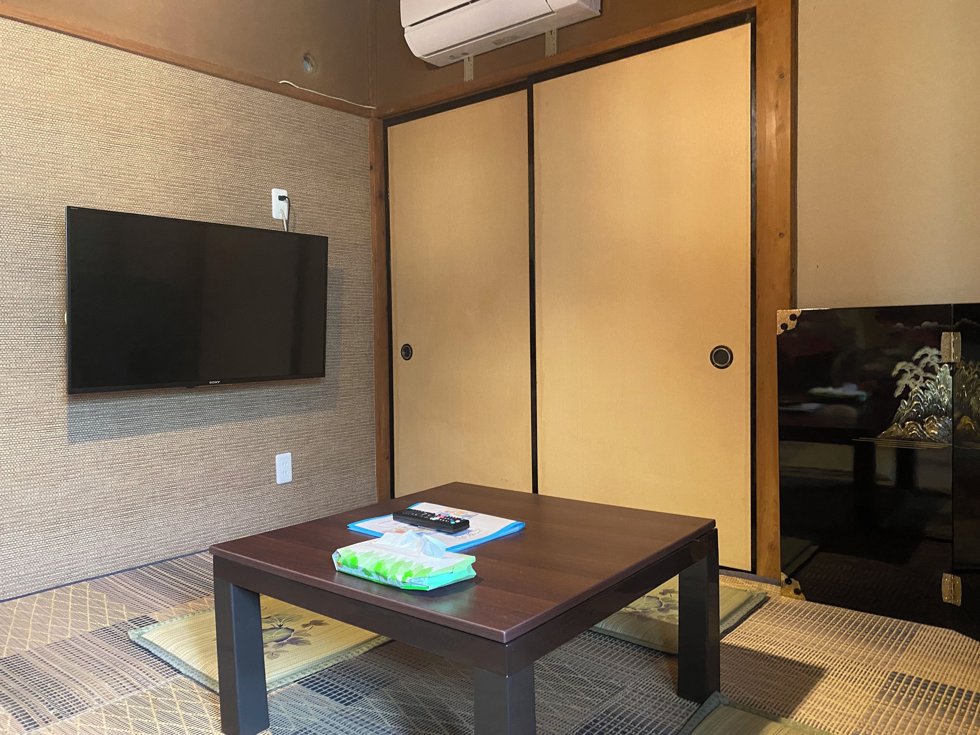 A room with a flat-screen TV mounted on a textured wall, a wooden table with a blue folder, and a sliding door with a decorative glass panel.