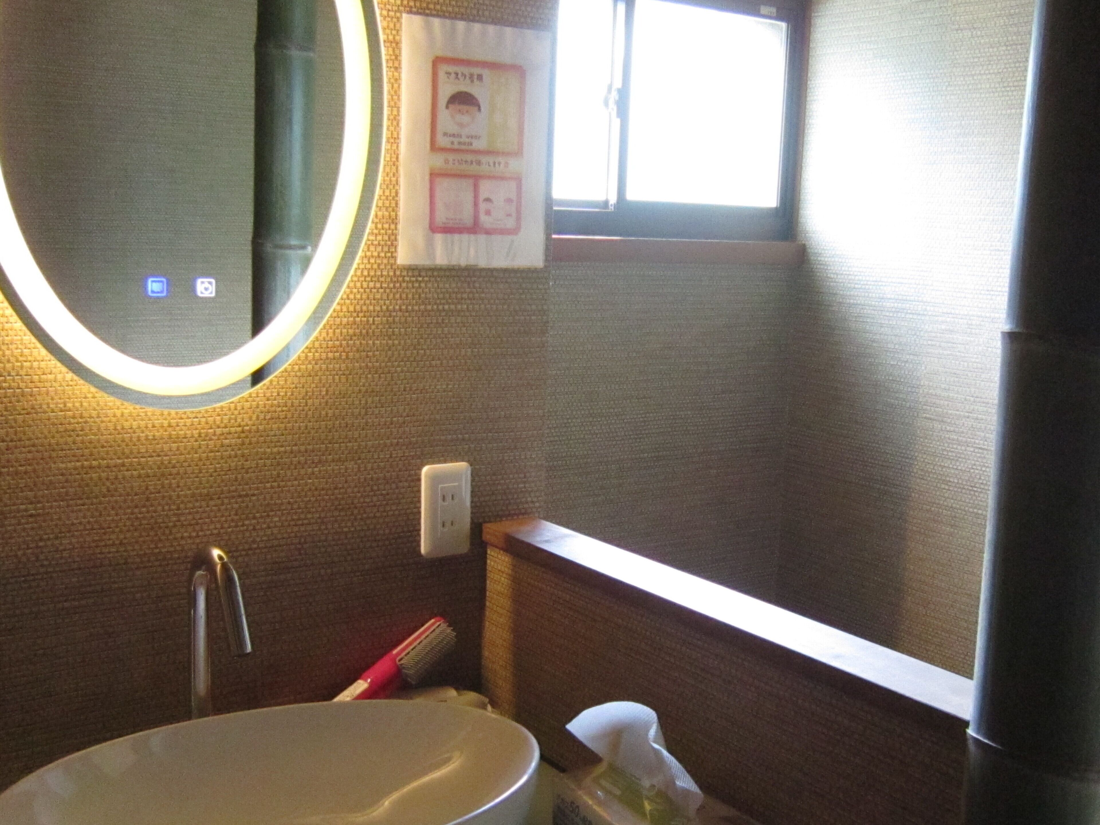 A bathroom with a round mirror, a sink, a window, and a towel rack.