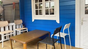 A dining area with a wooden table and chairs, a window with white shutters, and a blue wall. - BeachHouseNumazu (Numazu)