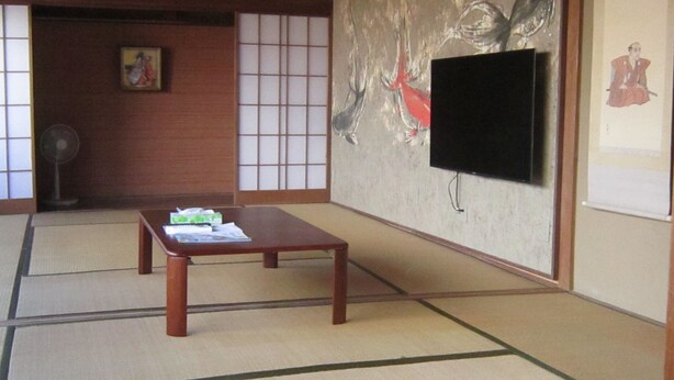 A traditional Japanese room with tatami flooring, a low wooden table, a TV mounted on the wall, and sliding shoji doors. - BeachHouseNumazu (Numazu)