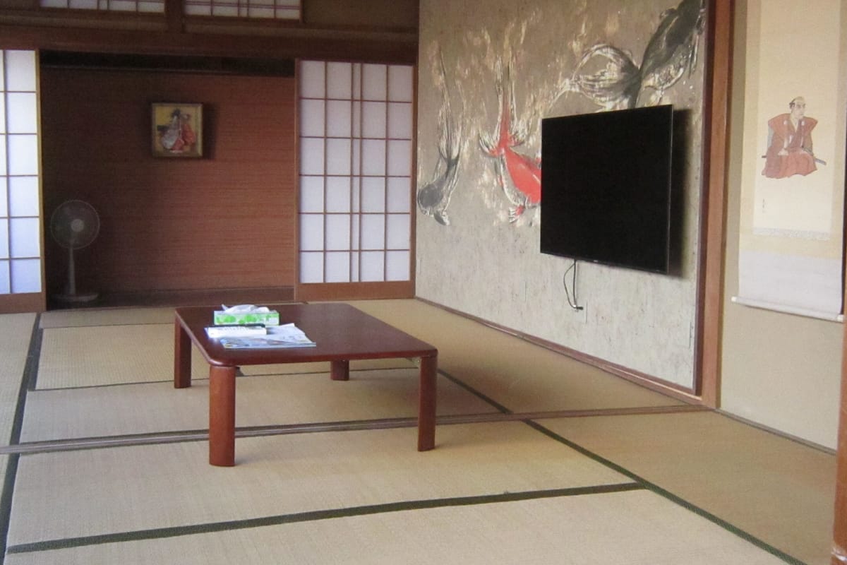 Una habitació japonesa tradicional amb paviment de tatami, una taula de fusta baixa, un televisor penjat a la paret i portes corredisses shoji.