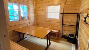 A wooden cabin interior with a dining table, two windows, a ceiling light, and a wall-mounted air conditioner. - BeachHouseNumazu (Numazu)