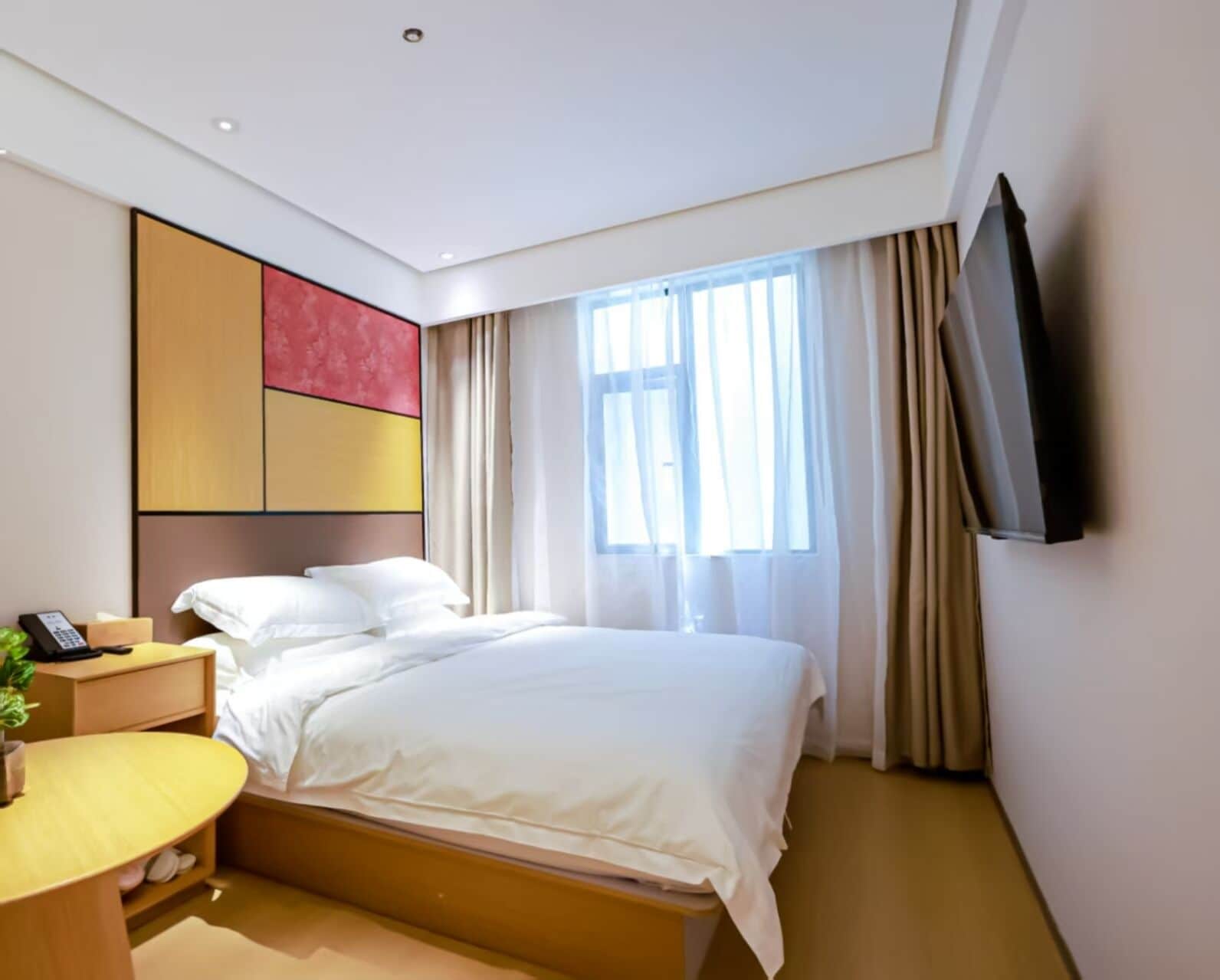 A hotel room with a bed, bedside table, and a TV mounted on the wall.