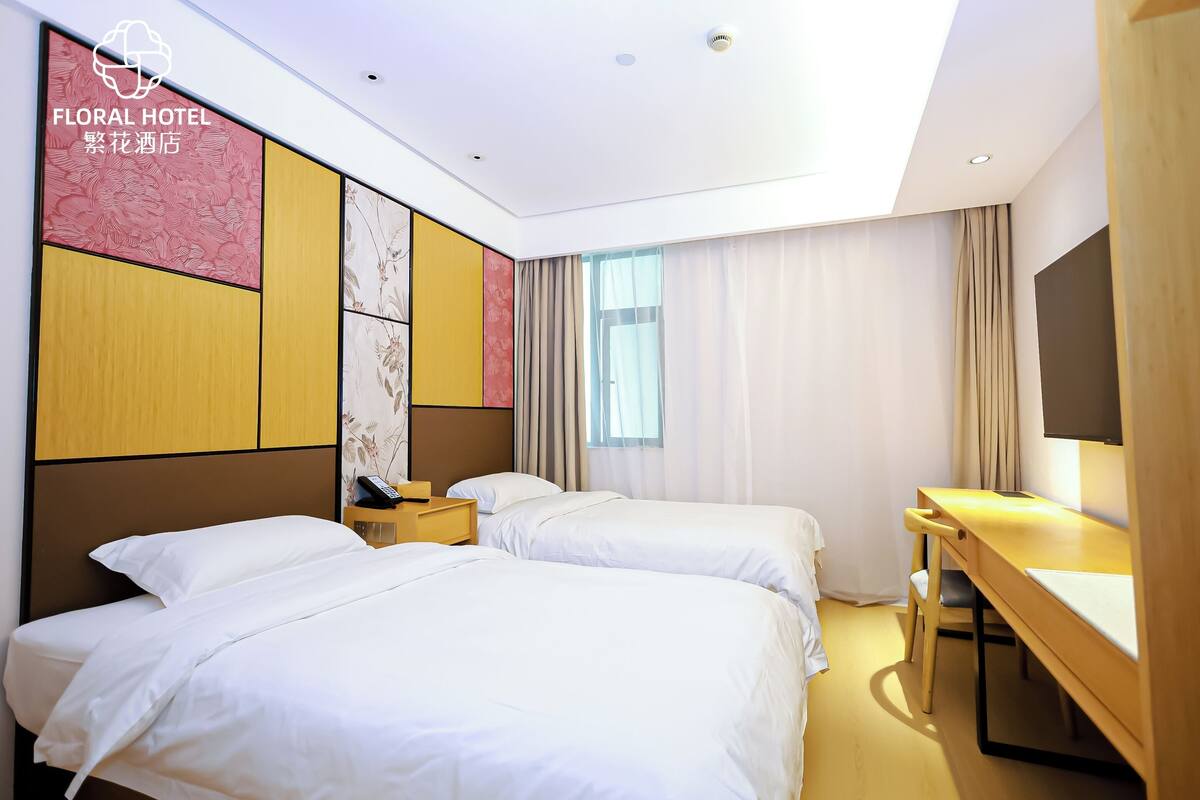 Quarto de hotel com duas camas, uma escrivaninha e uma janela grande.