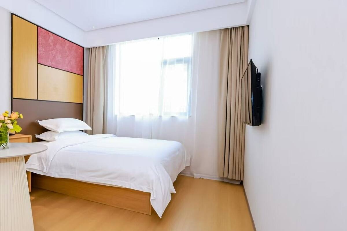 Quarto de hotel moderno com uma cama grande, uma TV de tela plana na parede e uma pequena mesa redonda com um vaso de flores.