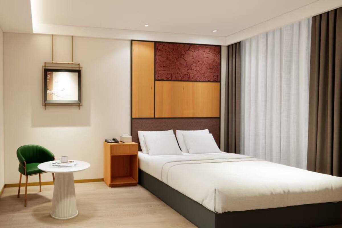 Quarto de hotel moderno com uma cama grande, uma mesa de cabeceira, uma cadeira verde e uma pequena mesa redonda.